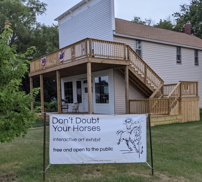 Exterior of the Masters Store and Hall in Walnut Grove, Minnesota, with banner outside inviting people to the Don't Doubt Your Horses art exhibit